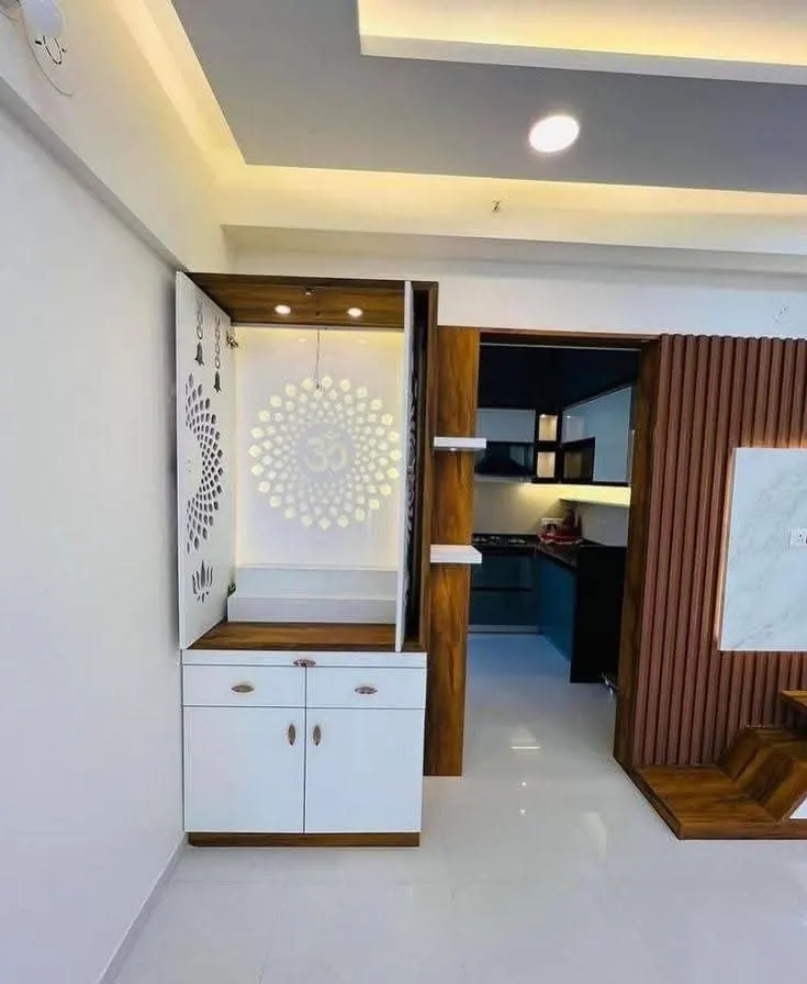 Wall-hung pooja mandir with a mandala door in an open living area beside a modular kitchen